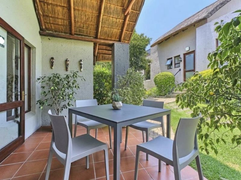 A covered patio area featuring terracotta tiling and a traditional thatched roof, providing a pleasant outdoor space overlooking the garden.