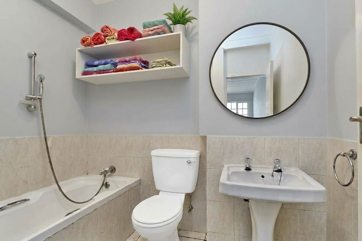 A functional bathroom featuring a bathtub with handheld shower, pedestal basin, toilet, and wall-mounted storage shelving.