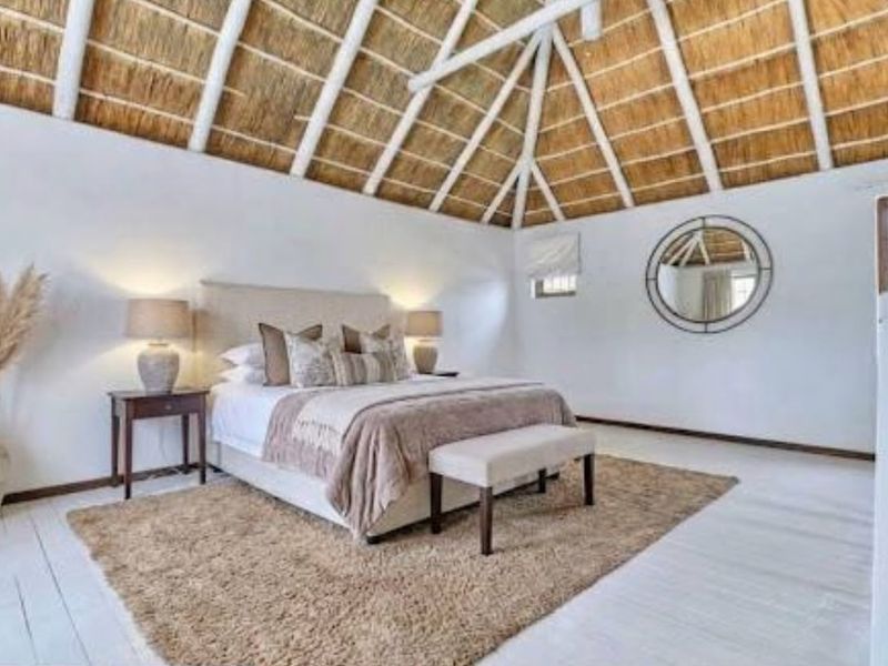 Spacious bedroom featuring a high vaulted exposed thatch ceiling with timber trusses and light-toned painted timber flooring.