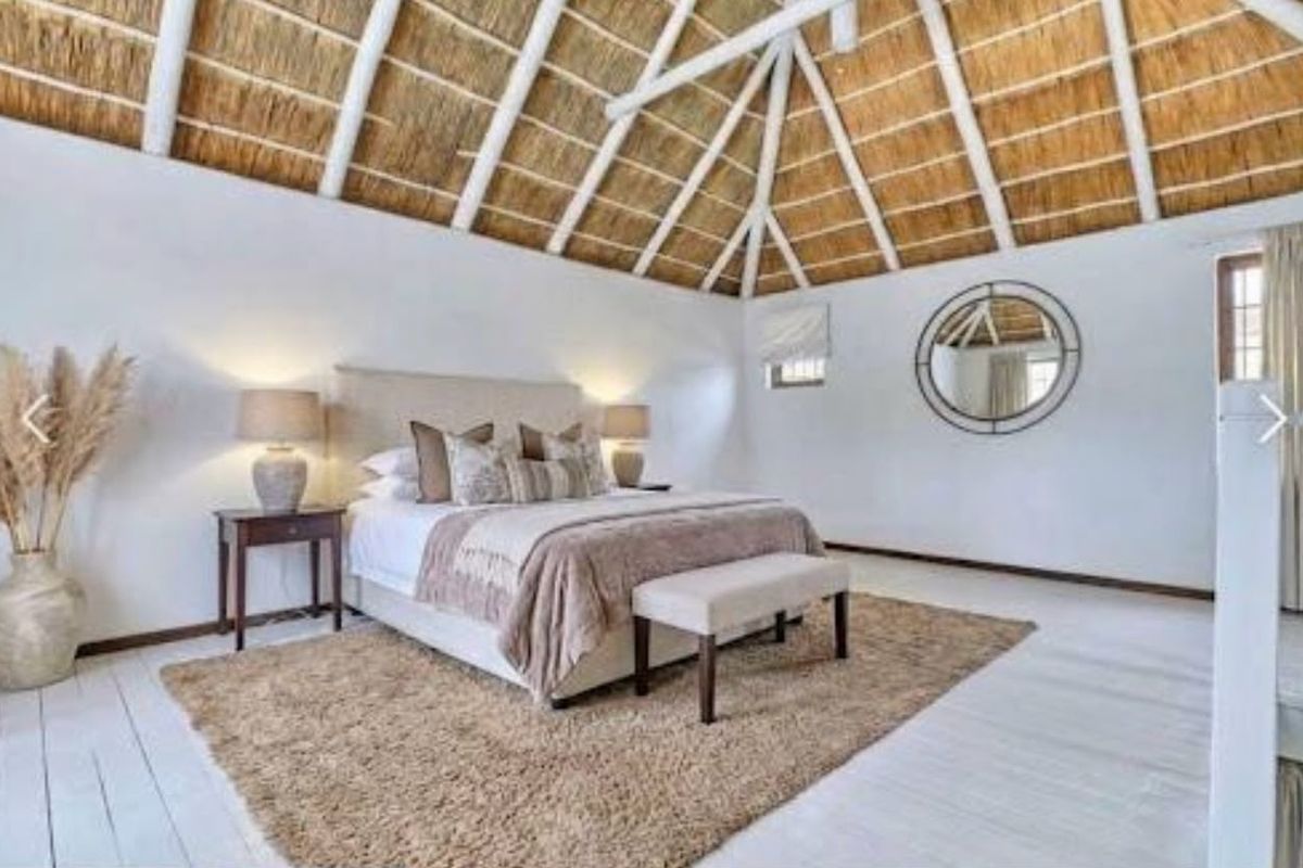 Spacious bedroom featuring a high vaulted exposed thatch ceiling with timber trusses and light-toned painted timber flooring.