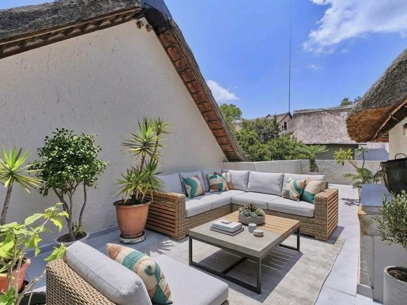 A spacious outdoor balcony featuring a traditional thatched roof, tiled flooring, and a parapet wall, offering a pleasant area for relaxation.