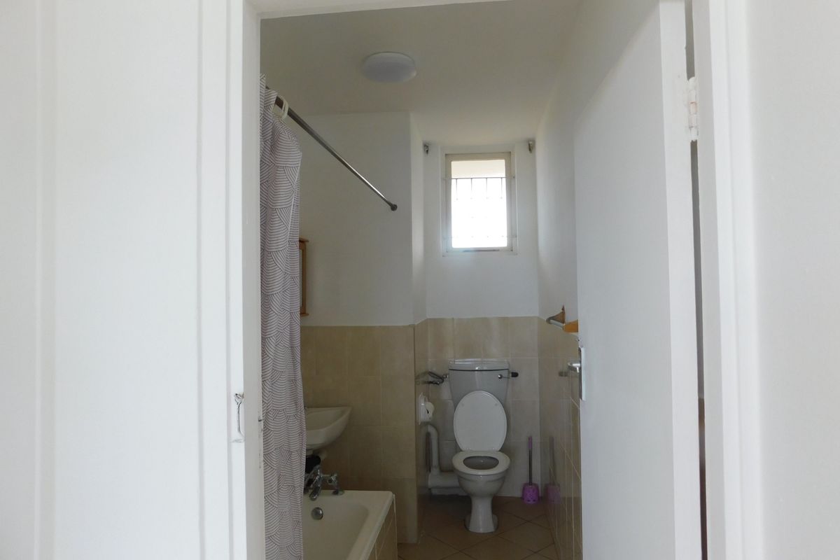 A functional bathroom featuring a bathtub, toilet, and basin with neutral wall and floor tiling.