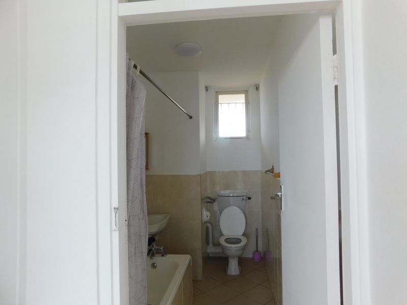 A functional bathroom featuring a bathtub, toilet, and basin with neutral wall and floor tiling.