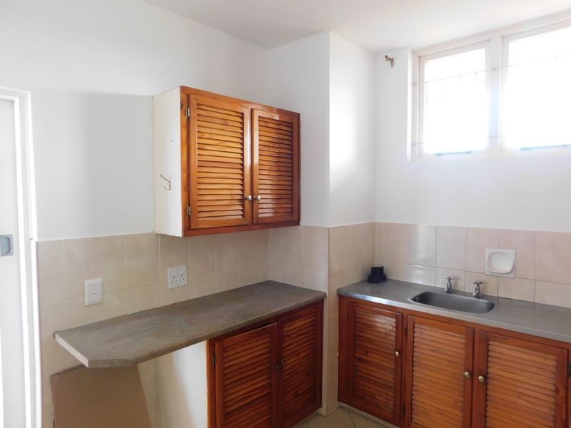 A functional scullery area featuring louvered wooden cabinetry, a stainless steel sink, and a tiled backsplash, offering potential for modernization.