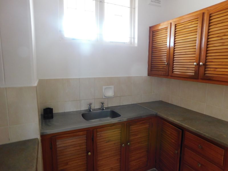 A functional scullery area featuring louvered wooden cabinetry, a stainless steel sink, and durable concrete countertops with a tiled backsplash.