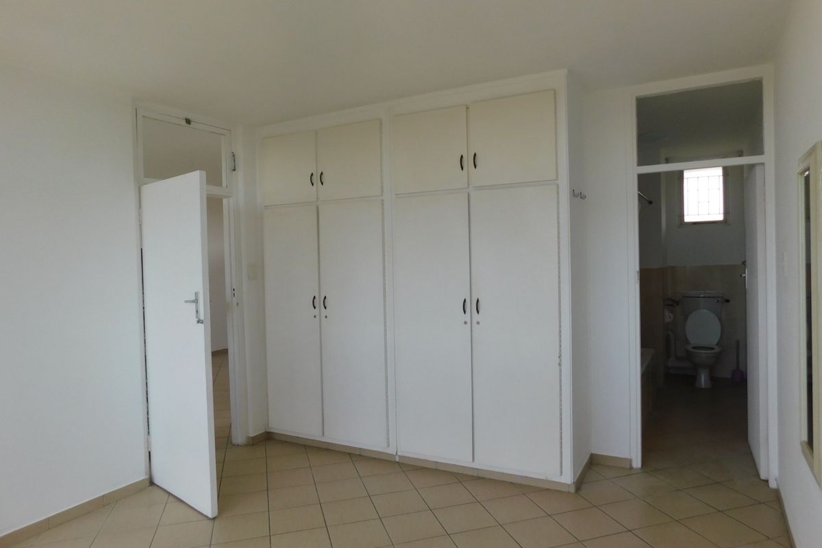 A spacious bedroom featuring neutral tiled flooring, ample built-in cupboard storage, and direct access to an en-suite bathroom.