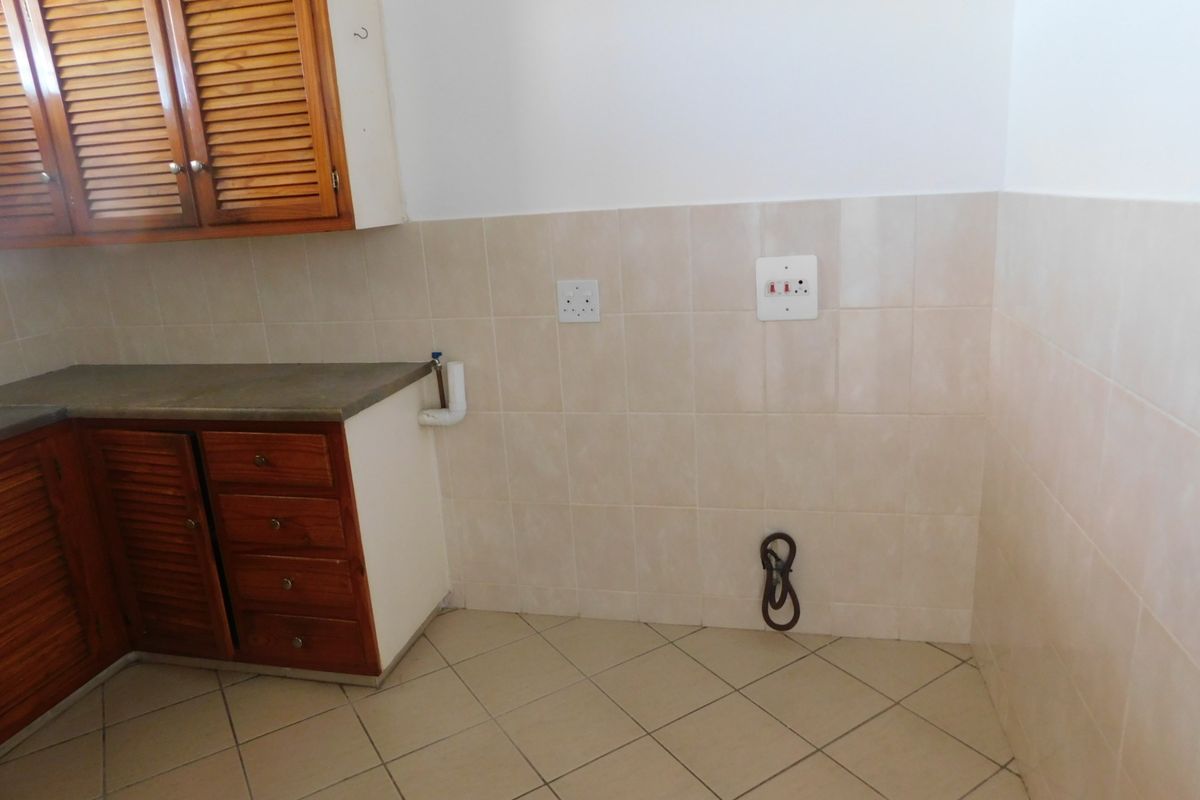 A functional kitchen area featuring wooden cabinetry, tiled backsplash, and tiled flooring with dedicated plumbing and electrical connections for appliances.