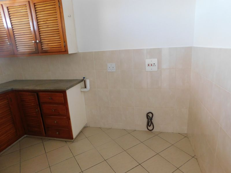 A functional kitchen area featuring wooden cabinetry, tiled backsplash, and tiled flooring with dedicated plumbing and electrical connections for appliances.