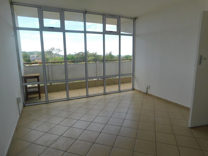 A bright, empty living area featuring large aluminium-framed windows that provide natural light and direct access to a private balcony with scenic views.