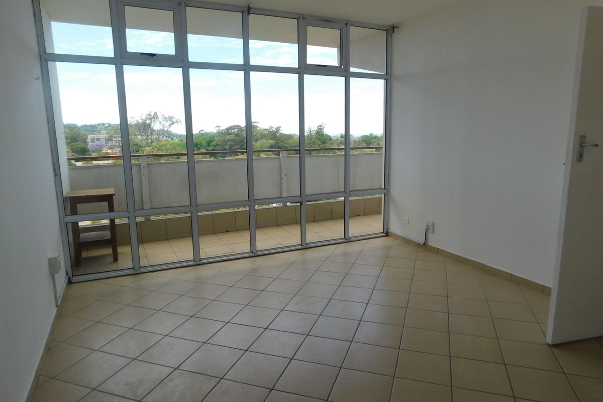 A bright, empty living area featuring large aluminium-framed windows that provide natural light and direct access to a private balcony with scenic views.