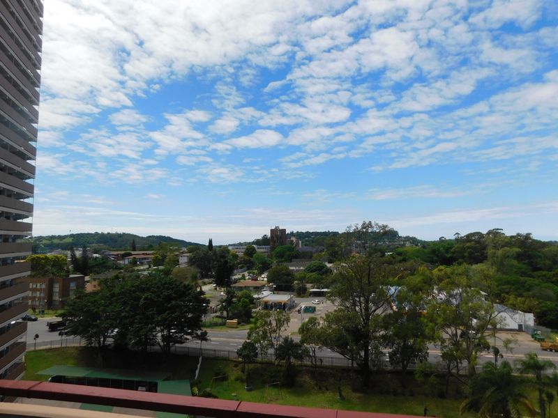 Elevated panoramic view overlooking the surrounding neighbourhood, lush greenery, and local infrastructure from an apartment balcony.