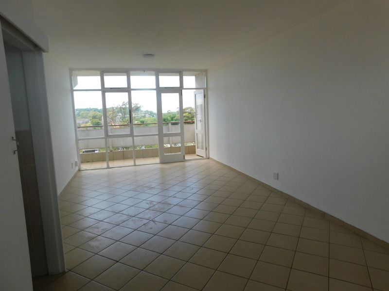 An empty, open-plan living area featuring neutral tiled flooring and large glass doors providing natural light and access to an outdoor balcony.