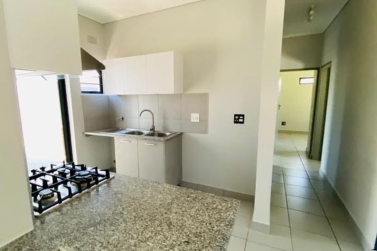 A clean, modern kitchen featuring granite countertops, a built-in gas hob with extractor, and tiled flooring, leading into a bright hallway.