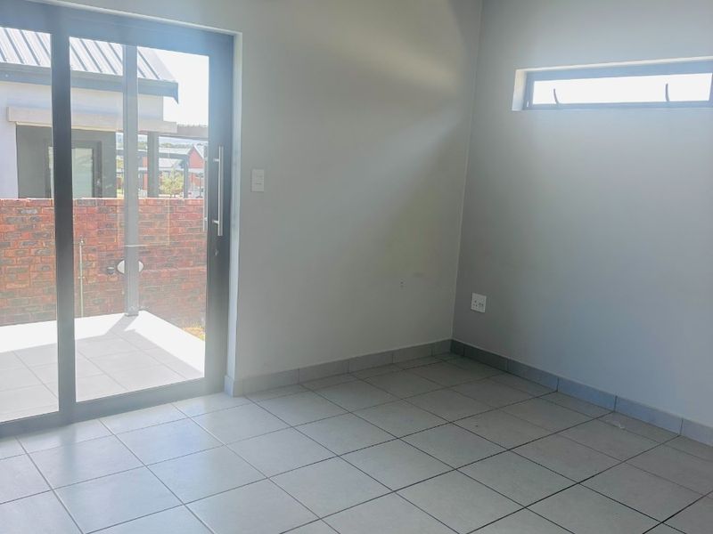 A bright, empty living area featuring neutral tiled flooring, a sliding glass door leading to the patio, and a modern horizontal window.