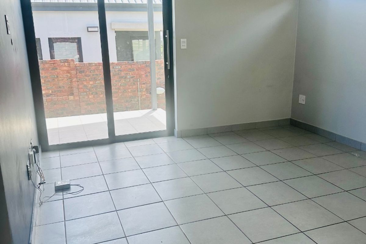A bright, empty living area featuring neutral tiled flooring, modern recessed lighting, and a large sliding glass door providing access to the outdoor patio.