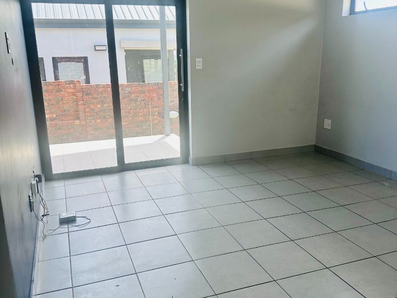 A bright, empty living area featuring neutral tiled flooring, modern recessed lighting, and a large sliding glass door providing access to the outdoor patio.