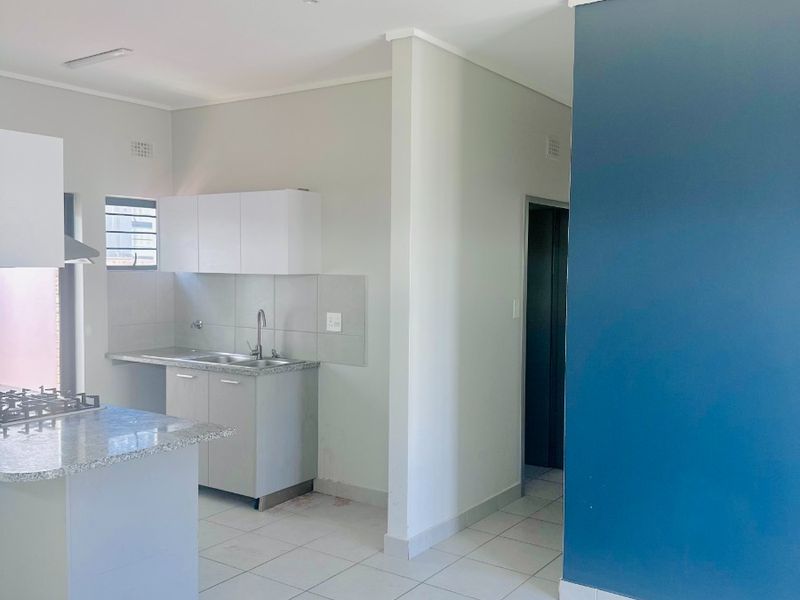 A clean, modern kitchen featuring granite countertops, built-in cabinetry, a gas hob with extractor, and neutral tiled flooring in an open-plan layout.