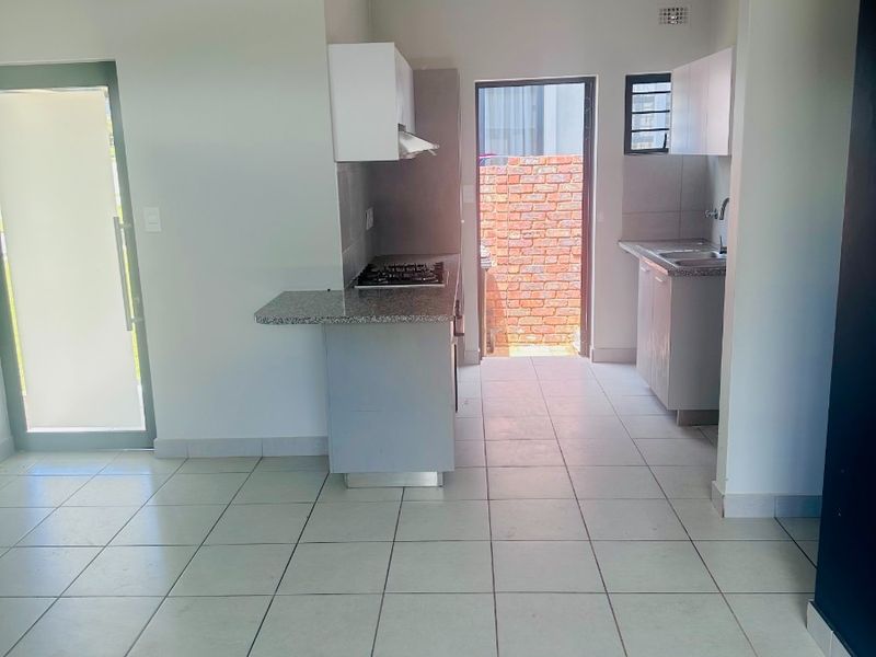 A clean, empty kitchen featuring granite countertops, a built-in gas hob with extractor, and tiled flooring, with direct access to an outdoor area.