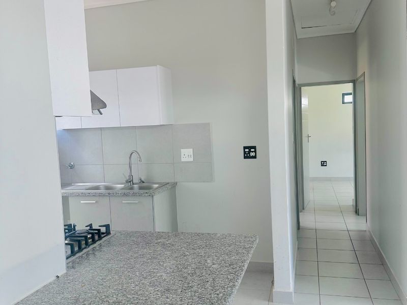 A clean, modern kitchen featuring granite countertops, a built-in gas hob, and tiled flooring, leading into a bright hallway.