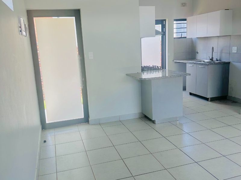 An open-plan kitchen area featuring granite countertops, built-in cabinetry, a gas hob, and ceramic floor tiles, leading to an exterior door.