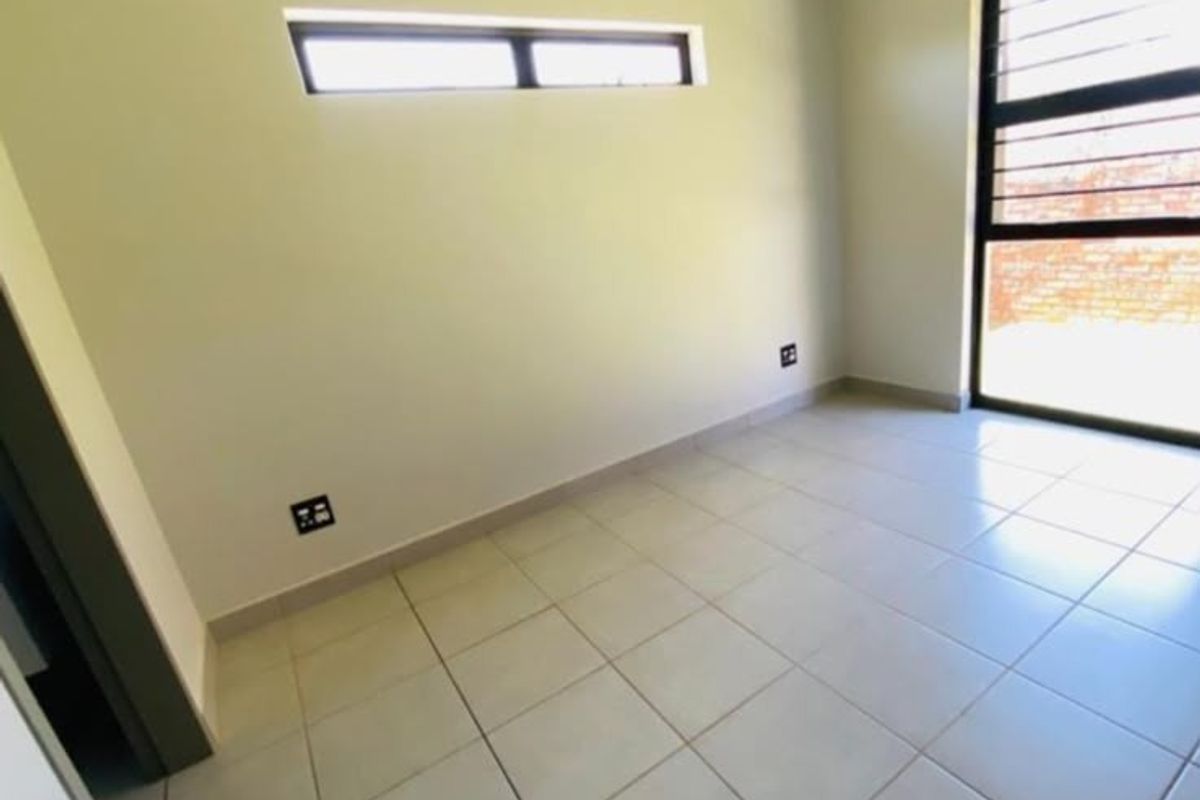 A bright, empty bedroom featuring neutral tiled flooring, a horizontal clerestory window, and a large window with security bars.
