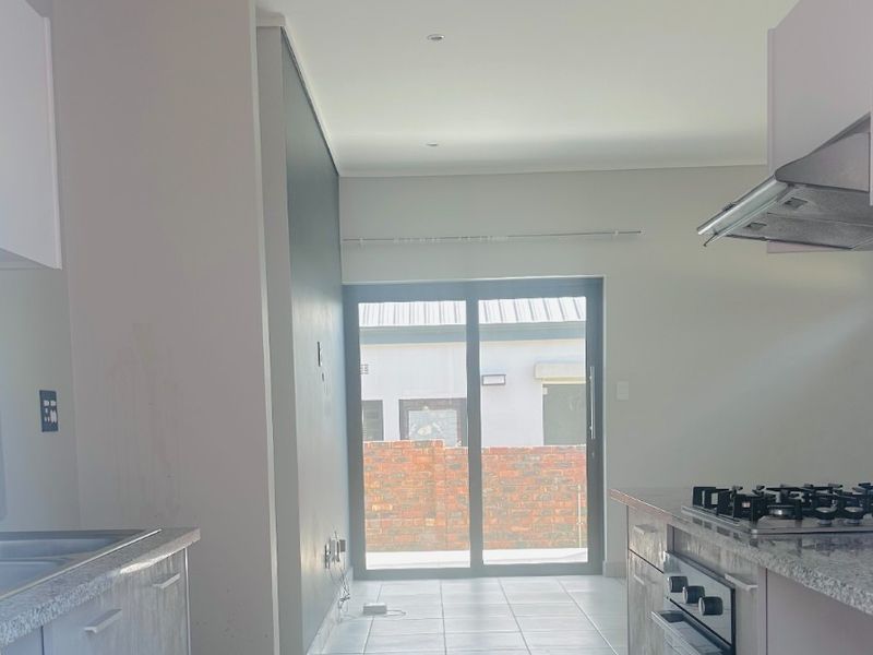 Modern kitchen featuring granite countertops, built-in oven, gas hob, and extractor fan, leading to an outdoor patio area through sliding glass doors.