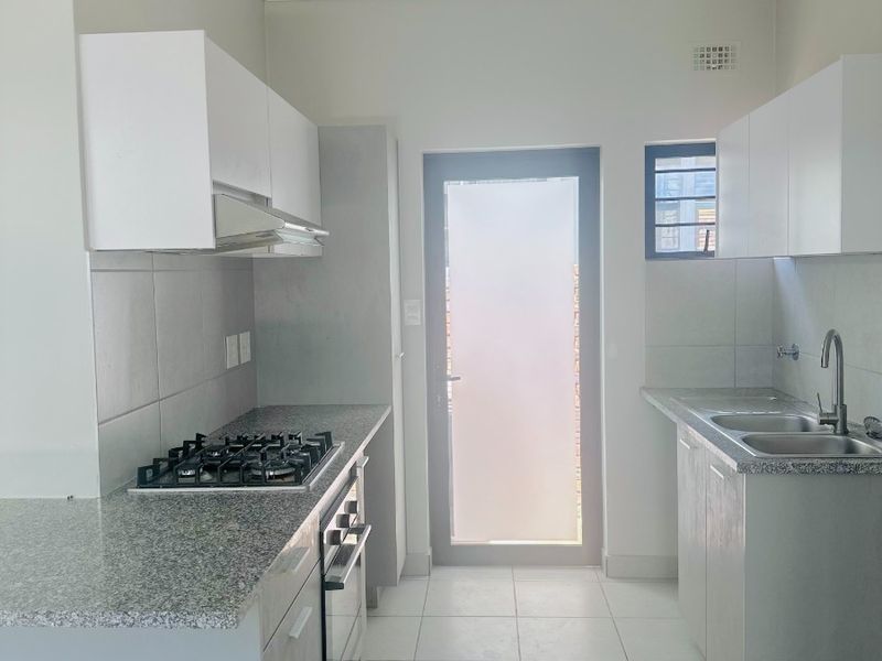 Modern kitchen featuring granite countertops, built-in gas hob, oven, extractor fan, and double sink with tiled flooring and direct access to the exterior.
