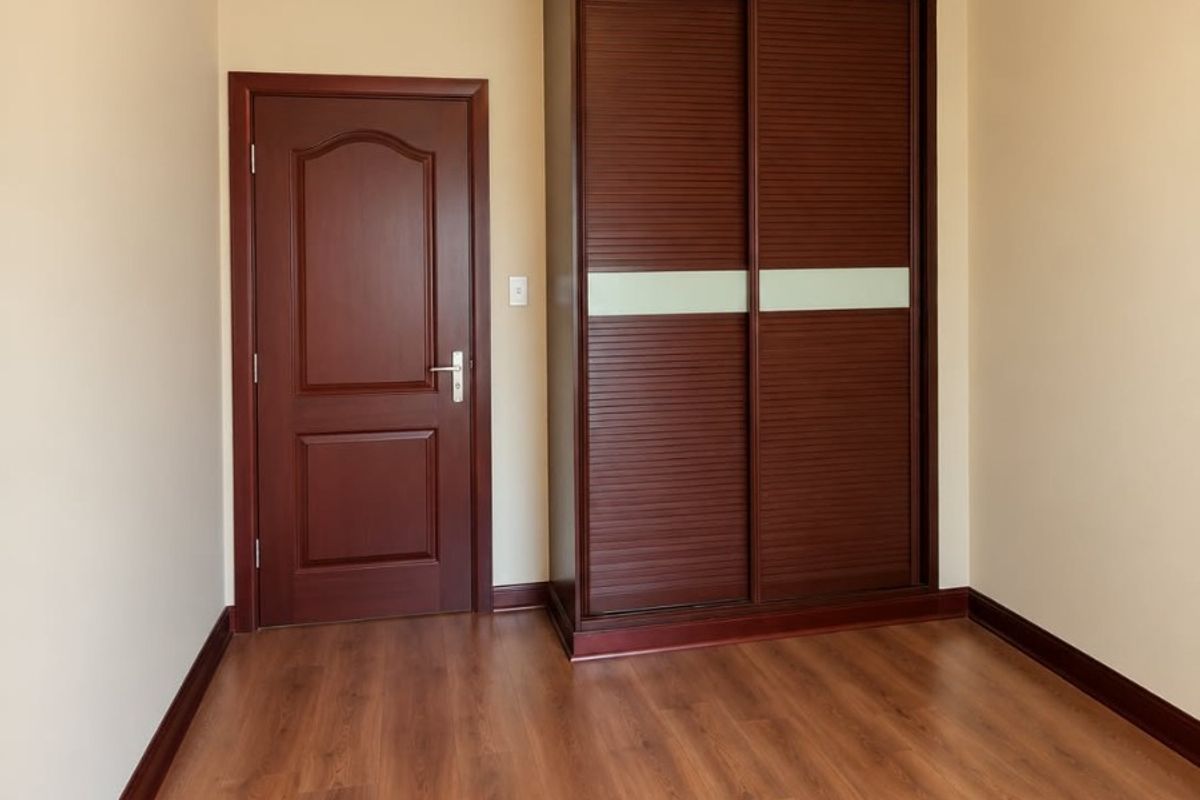 A clean, empty bedroom featuring warm-toned laminate flooring, dark wood trim, and a built-in sliding door wardrobe.