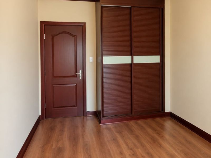 A clean, empty bedroom featuring warm-toned laminate flooring, dark wood trim, and a built-in sliding door wardrobe.