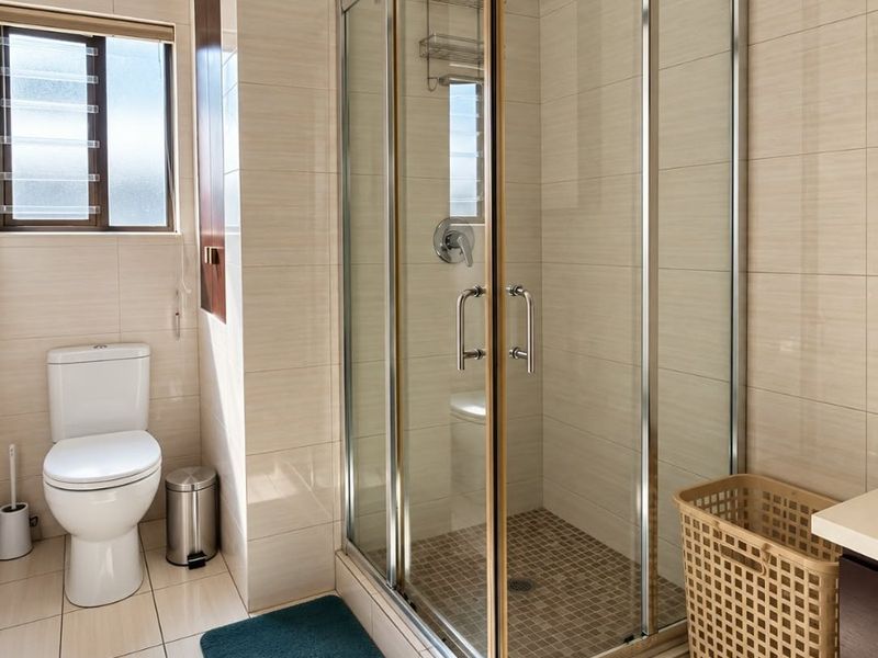 A clean, well-maintained bathroom featuring a glass-enclosed shower, modern toilet, and neutral floor-to-ceiling wall tiles.