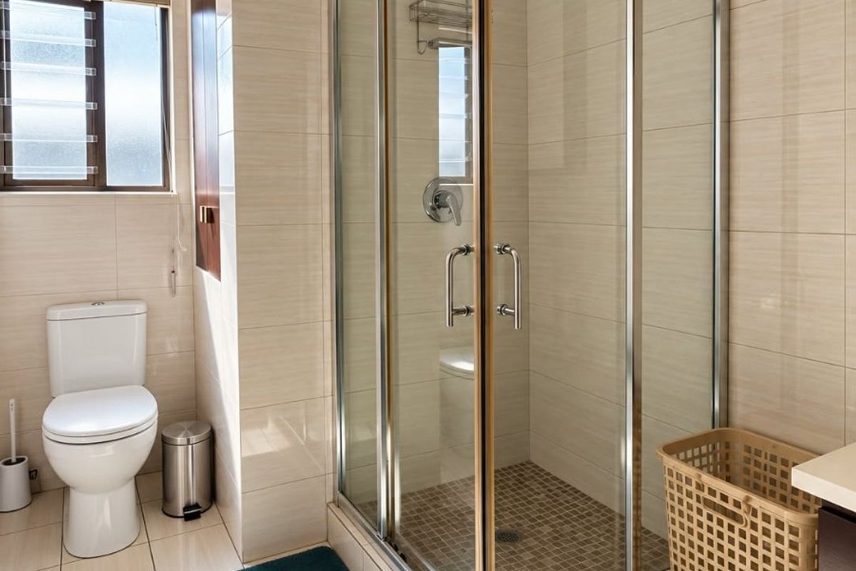 A clean, well-maintained bathroom featuring a glass-enclosed shower, modern toilet, and neutral floor-to-ceiling wall tiles.