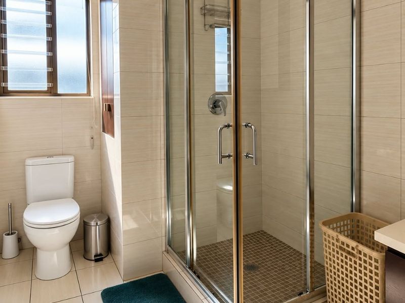 A well-maintained bathroom featuring a glass-enclosed shower, tiled flooring, and neutral wall tiles, providing a clean and functional space.