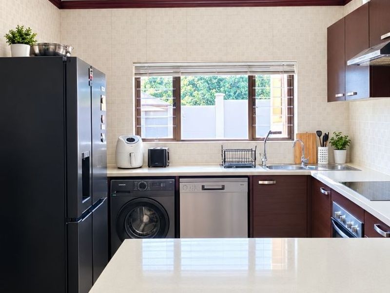 A well-maintained kitchen featuring dark wood cabinetry, stone countertops, integrated appliances, and a tiled backsplash with a window overlooking the exterior.