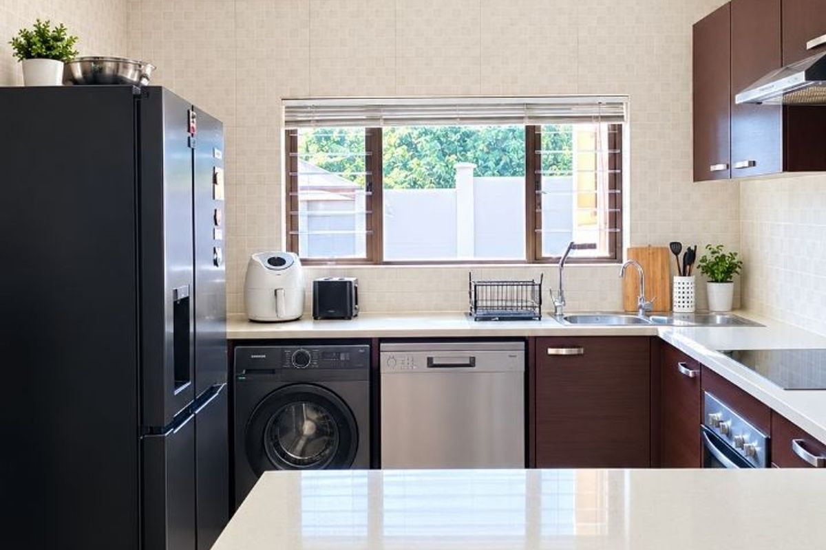 A well-maintained kitchen featuring dark wood cabinetry, stone countertops, integrated appliances, and a tiled backsplash with a window overlooking the exterior.