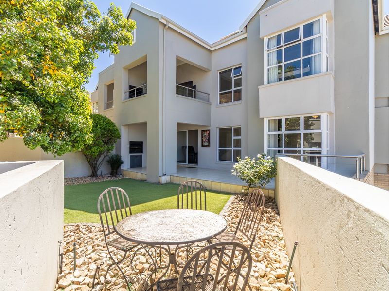 Rear view of the apartment complex featuring a private garden area, tiled patio with built-in braai, and upper-level balconies.