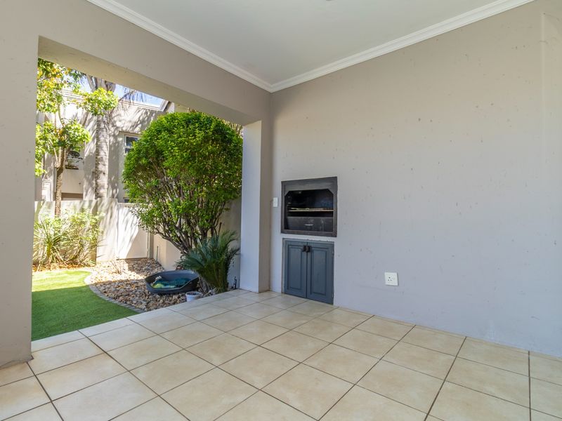 Covered patio area featuring tiled flooring and a built-in braai, providing a functional outdoor space for entertaining.