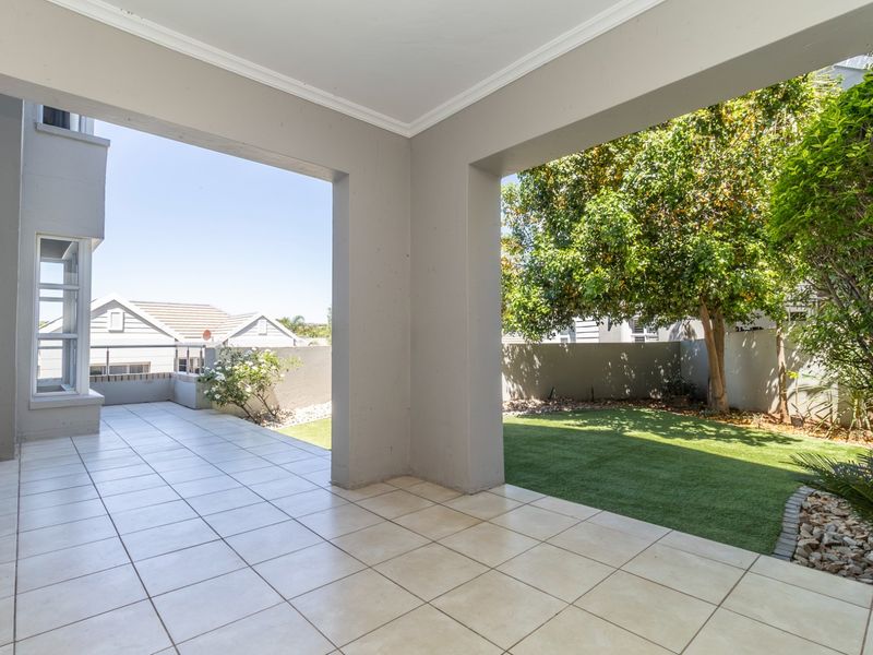 A spacious covered patio featuring tiled flooring, overlooking a private garden area with artificial lawn and boundary walls.