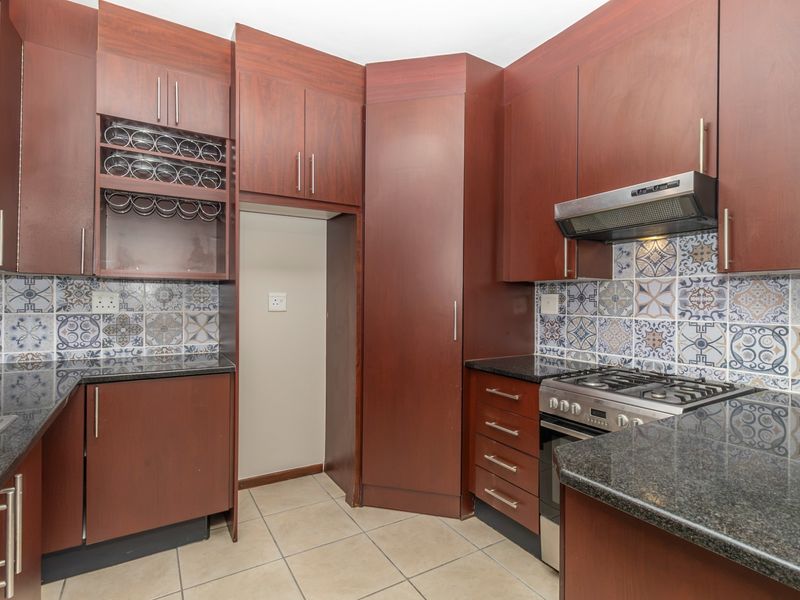 A well-maintained kitchen featuring dark wood cabinetry, granite countertops, a gas hob with extractor fan, and decorative patterned tile backsplash.
