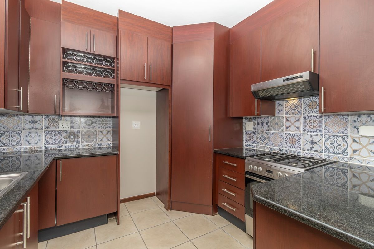 A well-maintained kitchen featuring dark wood cabinetry, granite countertops, a gas hob with extractor fan, and decorative patterned tile backsplash.