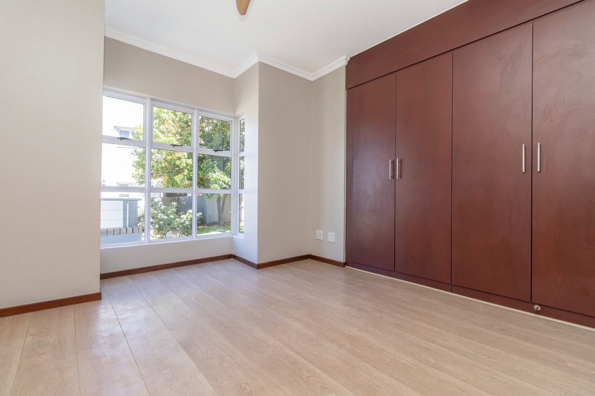 A bright, empty bedroom featuring light laminate flooring, neutral walls, and large built-in wooden cupboards.