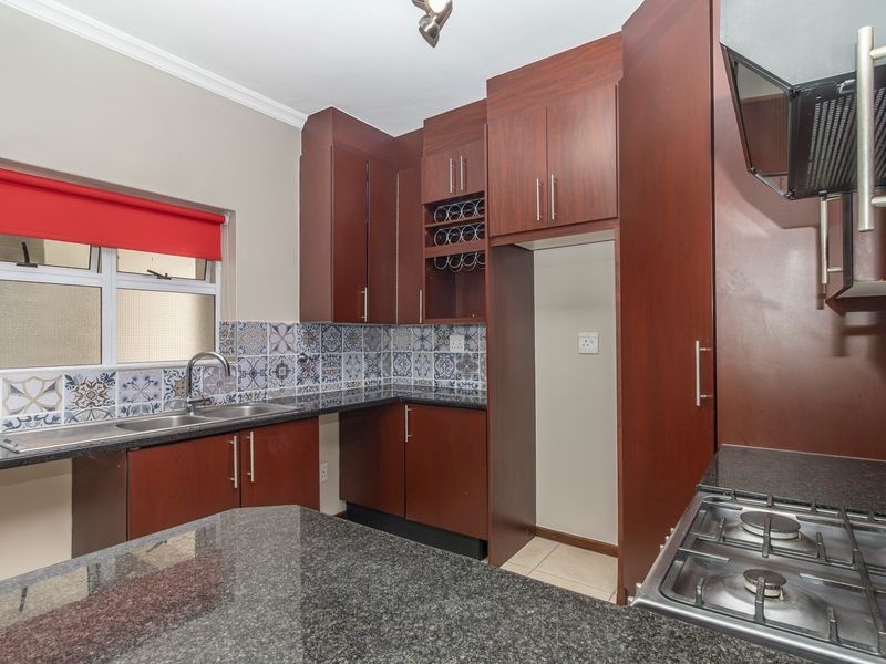 A functional kitchen featuring dark wood cabinetry, granite countertops, a gas hob with extractor fan, and decorative tiled backsplash.