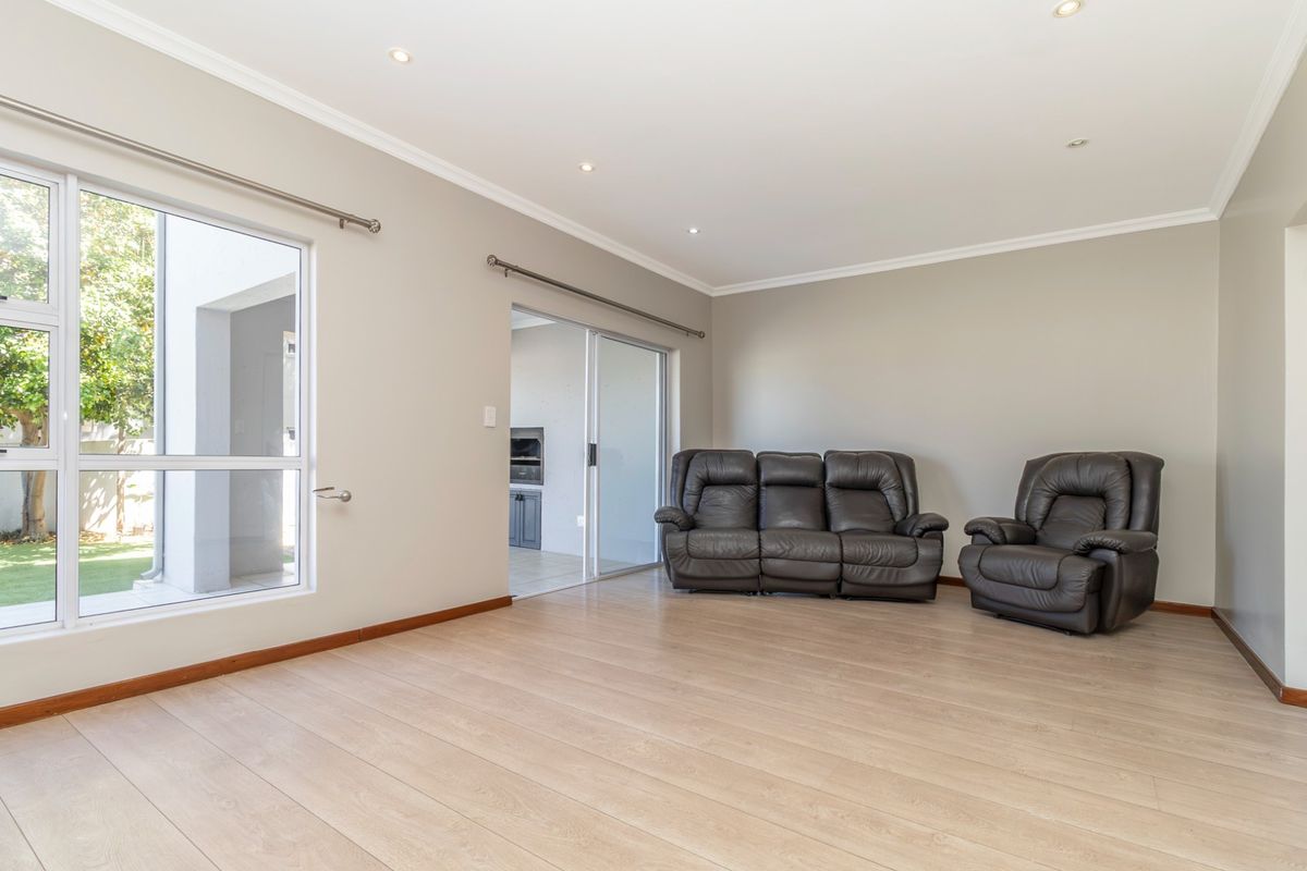 A bright and spacious living area featuring light-toned laminate flooring, recessed downlighting, and large windows providing natural light and access to the outdoor area.