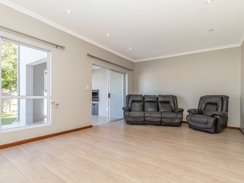 A bright and spacious living area featuring light-toned laminate flooring, recessed downlighting, and large windows providing natural light and access to the outdoor area.