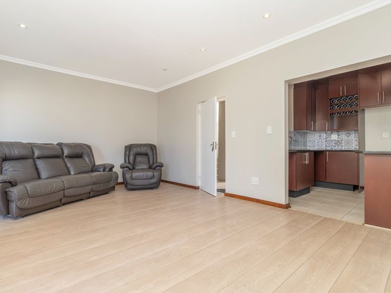 Open-plan living area featuring light laminate flooring and recessed lighting, seamlessly connected to a compact kitchen with dark wood cabinetry and decorative backsplash.