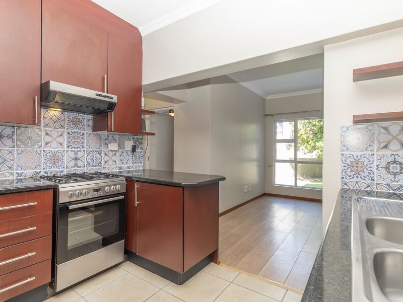 A functional kitchen featuring dark wood cabinetry, granite countertops, a stainless steel stove with extractor, and decorative patterned tile backsplash, opening into a living area.