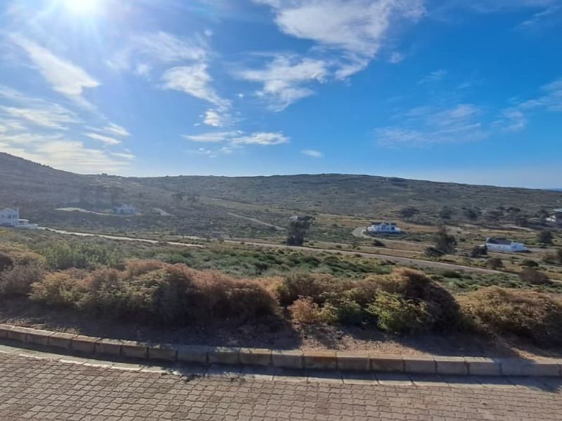 A wide-angle view of the surrounding coastal landscape and residential area, featuring natural vegetation and paved road infrastructure.