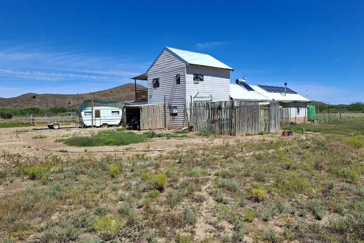 Rear view of a rural farm property featuring timber siding, solar energy infrastructure, and a corrugated metal roof set within a large open landscape.