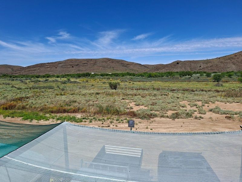 Expansive rural landscape view featuring natural vegetation and distant mountain ranges, viewed from under a protective shade net structure.