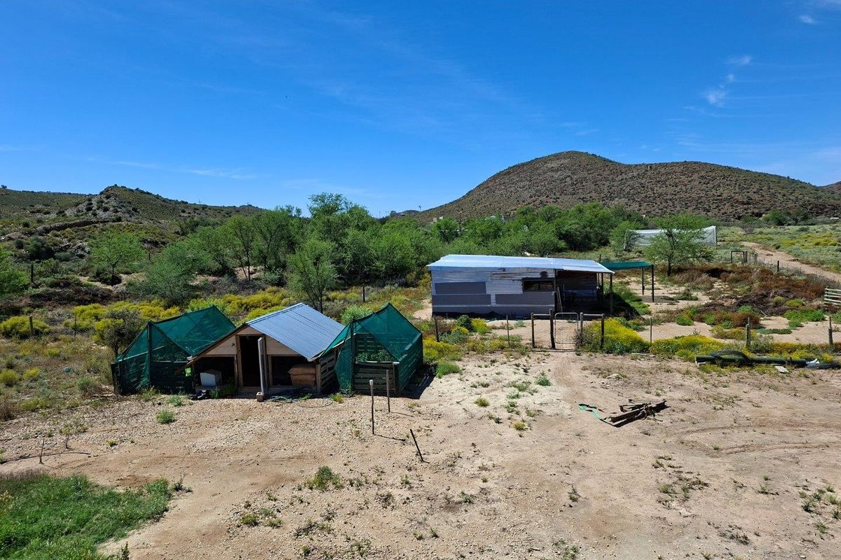 Aerial view of a rural farm property featuring basic outbuildings, corrugated metal roofing, and fenced enclosures set within a natural landscape.
