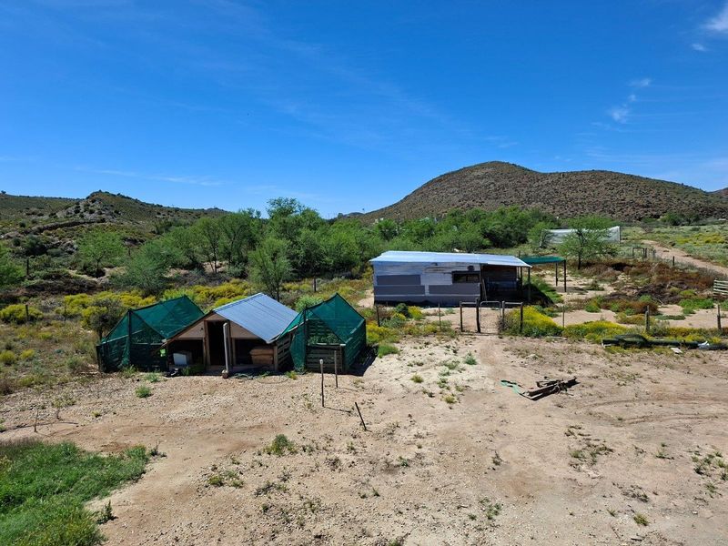 Aerial view of a rural farm property featuring basic outbuildings, corrugated metal roofing, and fenced enclosures set within a natural landscape.